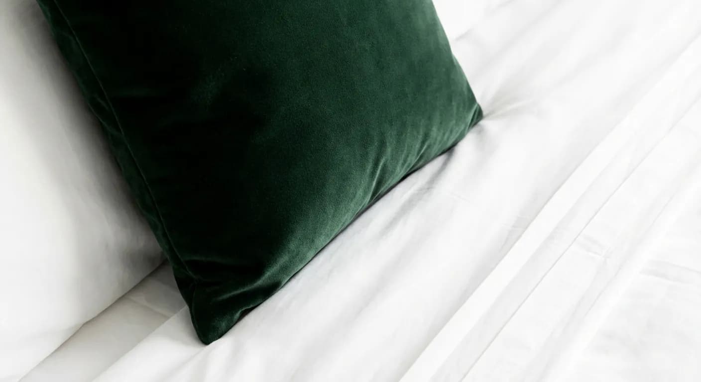 Détail minimaliste d'un coussin vert forêt sur des draps blancs