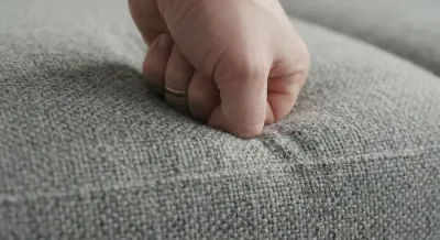 Gros plan sur la texture d'un tissu de canapé et test de résilience de la mousse sous la pression d'une main.