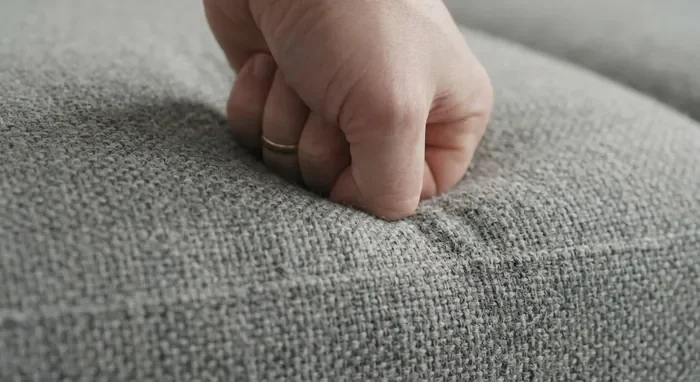 Densité canapé Poltronesofa : guide 2026 - 3 secrets contre l'affaissement - Quelle densité pour votre Poltronesofa ? Gros plan sur la texture d'un tissu de canapé et test de résilience de la mousse sous la pression d'une main.