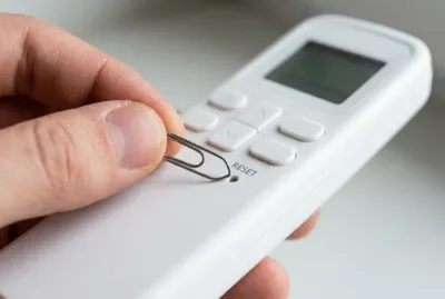 Main avec un trombone réinitialisant une télécommande de climatiseur Toshiba